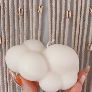 May include: A white cloud-shaped candle with a textured surface. The candle is being held by a hand with a silver ring.