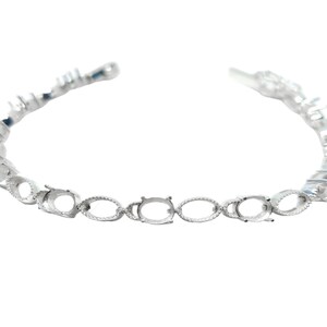 May include: Silver bracelet with oval-shaped settings for gemstones. The bracelet is made of a delicate chain with a clasp closure.
