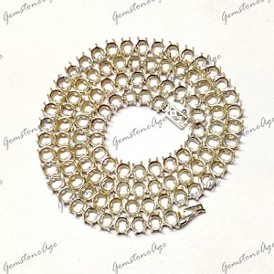 Puede incluir: Una cadena de plata con múltiples engastes redondos para piedras preciosas. La cadena está dispuesta en círculo sobre una superficie blanca.