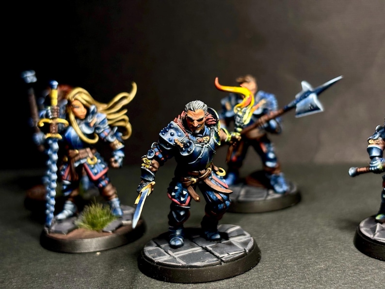 May include: Four miniature figures painted in a fantasy style. The figures are wearing armor and holding weapons. The figures are standing on circular bases.