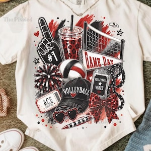 May include: An off-white t-shirt featuring a graphic print of volleyball-themed items including a number one foam finger, a leopard print cup, a volleyball net, a pennant reading GAME DAY, a pom-pom, a volleyball, a cap, and a bow.