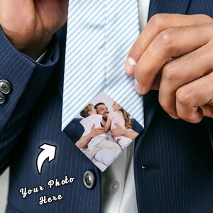 Può includere: Una cravatta a righe bianche e azzurre con una foto di famiglia personalizzata. La cravatta è tenuta da una persona che indossa un abito blu navy. Il testo "Your Photo Here" è visibile sull'abito.
