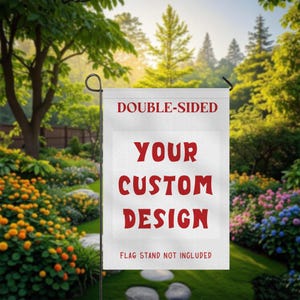 May include: A white, double-sided garden flag with the text "DOUBLE-SIDED" at the top and "YOUR CUSTOM DESIGN" in red block letters. The bottom of the flag reads "FLAG STAND NOT INCLUDED". The flag is displayed in a lush garden setting.