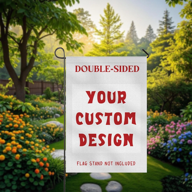 May include: A white, double-sided garden flag with the text "DOUBLE-SIDED" at the top and "YOUR CUSTOM DESIGN" in red block letters. The bottom of the flag reads "FLAG STAND NOT INCLUDED". The flag is displayed in a lush garden setting.