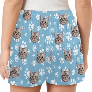 Op de afbeelding: Blauwe sport shorts met een wit pootprint en kattengezicht patroon.