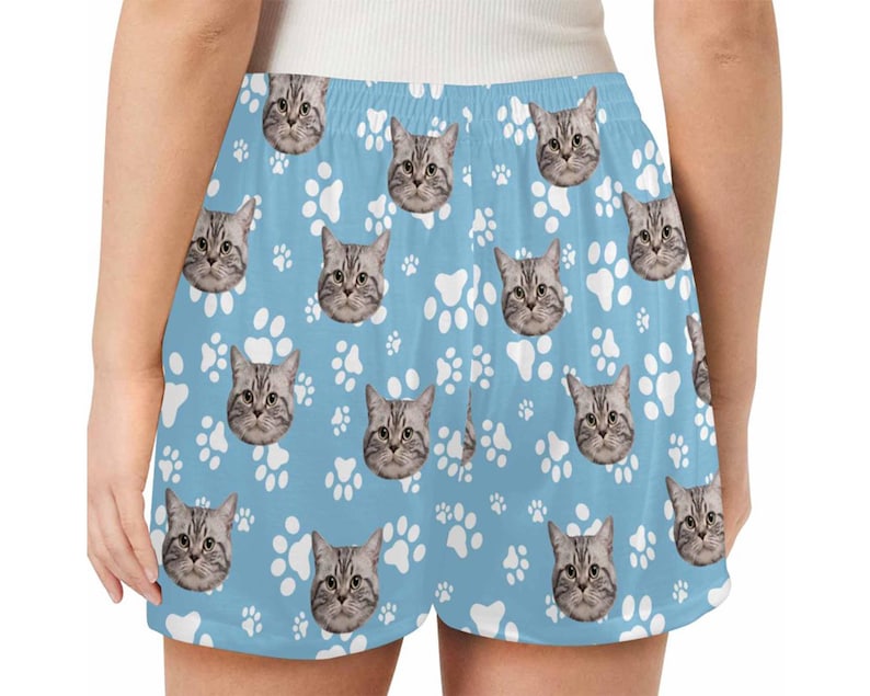Op de afbeelding: Blauwe sport shorts met een wit pootprint en kattengezicht patroon.