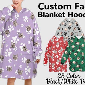 Pode incluir: Uma jaqueta de cobertor com capuz roxa com um padrão de pata branca e rosto de gato. O texto "Custom Face Blanket Hoodie" e "28 Color Black/White Paw" é exibido abaixo da imagem.