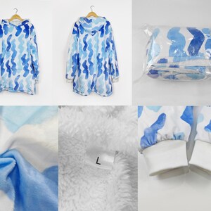 Puede incluir: Una manta con capucha azul y blanca con un patr&oacute;n ondulado. La manta est&aacute; hecha de suave felpa y tiene una capucha grande. La manta se muestra doblada y en una bolsa de pl&aacute;stico.