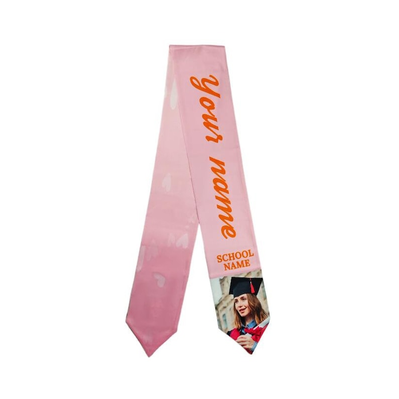 May include: Pink graduation sash with the text "Your name" and "School Name" in orange. A photo of a graduate wearing a cap and gown is printed on the sash.