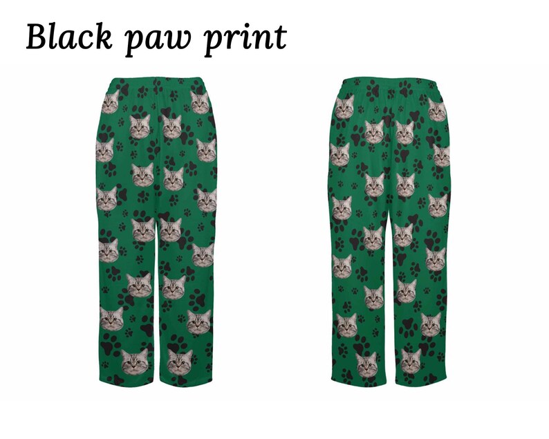 Op de afbeelding: Groene pyjamabroek met een zwarte pootprint en een kattengezichtpatroon. De tekst "Black paw print" staat bovenaan de afbeelding.