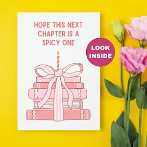 May include: A white card with pink and white illustrations of a stack of books tied with a pink ribbon and a lit candle on top. The text on the card reads "Hope this next chapter is a spicy one." There is a pink circle on the card that says "Look inside."