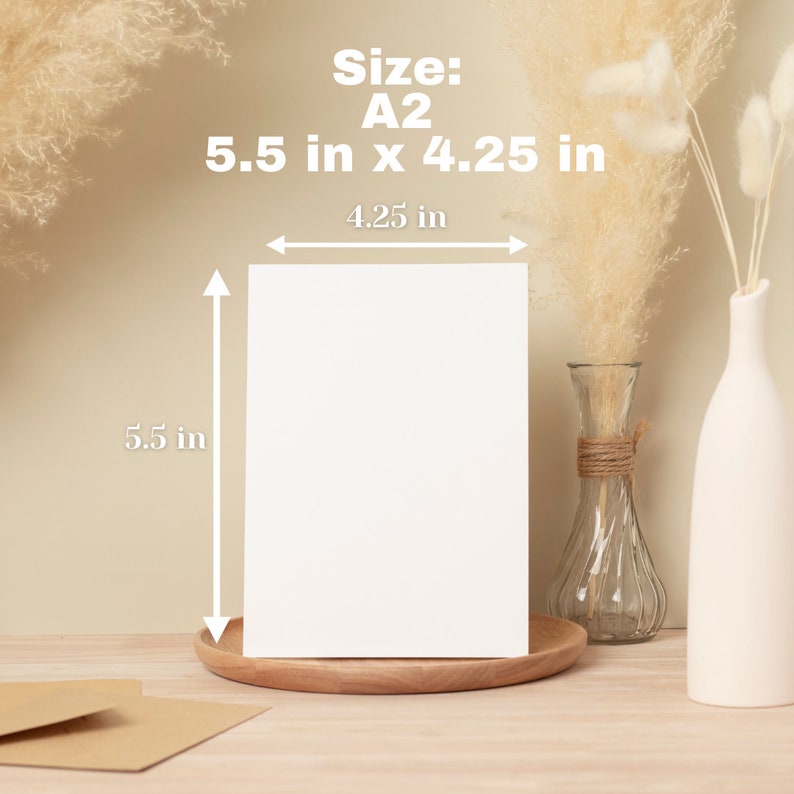 May include: A white A2 size card, 5.5 inches by 4.25 inches, is displayed on a wooden tray. The image includes a clear glass vase with twine and a white ceramic vase, along with dried decorative plants. The background is a neutral beige.
