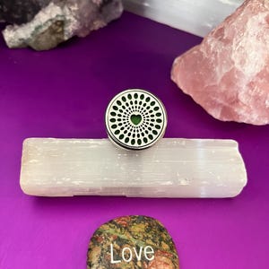 May include: A silver diffuser locket with a green heart design. The locket is sitting on a white selenite crystal. The word "Love" is written on a small, multi-colored stone.