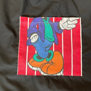 May include: Black tote bag with a red and white striped pocket featuring a cartoon character wearing a blue jacket, green shirt, and orange shoes.