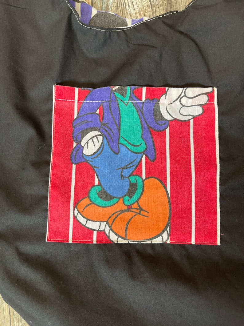 May include: Black tote bag with a red and white striped pocket featuring a cartoon character wearing a blue jacket, green shirt, and orange shoes.