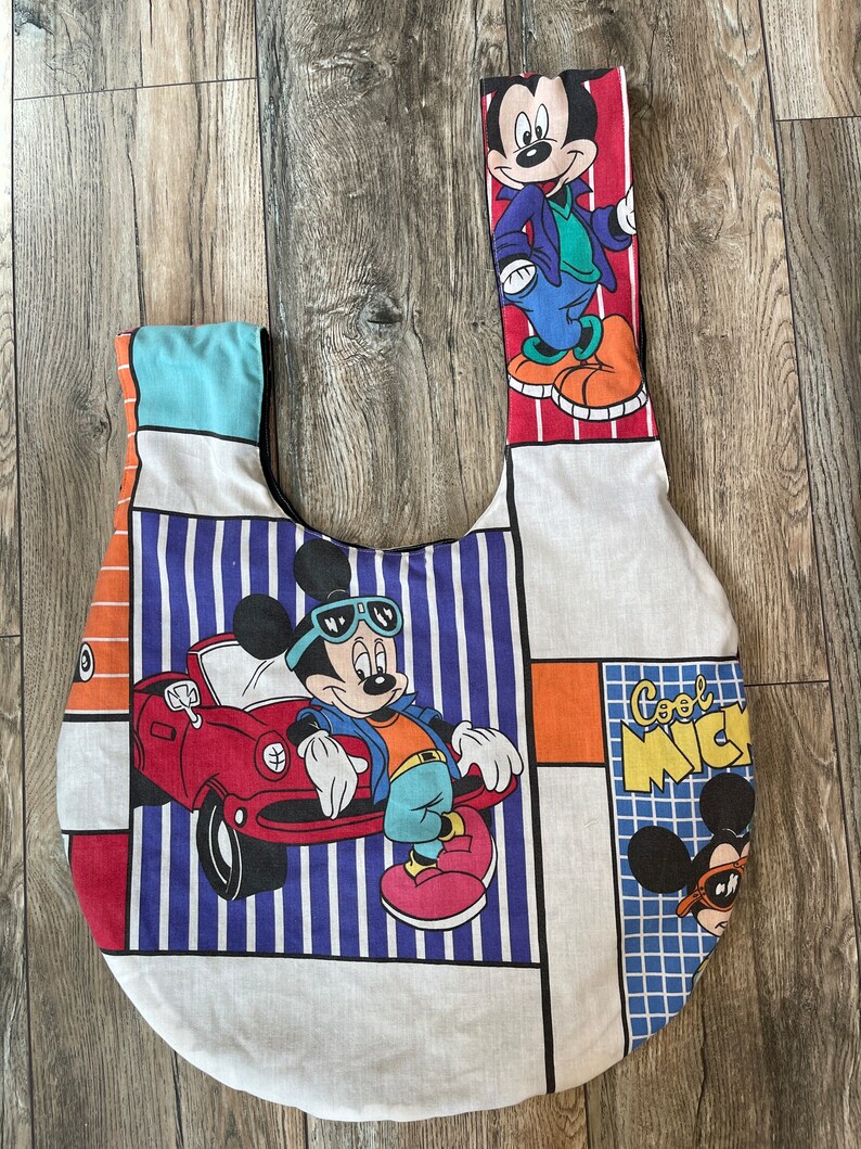 May include: A white fabric tote bag with a patchwork design featuring Mickey Mouse in different poses. The bag has a blue and white striped section, a red and orange section, and a blue and white checkered section. The bag also features the text "Cool Mickey".