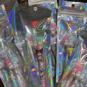 May include: A set of five holographic plastic bags containing colorful pens with character designs. The pens are packaged in a woven basket.