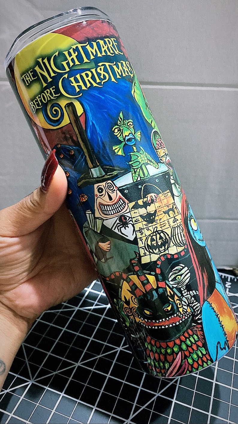 K&ouml;nnte beinhalten: Ein zylindrischer Becher mit einem farbenfrohen Design aus "The Nightmare Before Christmas". Der Becher zeigt Charaktere und Szenen aus dem Film, wobei der Titel deutlich sichtbar ist. Das Design umfasst eine Vielzahl von Farben, darunter Blau, Rot und Gr&uuml;n.