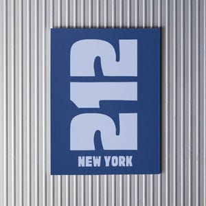 Puede incluir: Una tarjeta azul con el número "212" en blanco, en negrita. El texto "NEW YORK" está impreso en blanco debajo del número.
