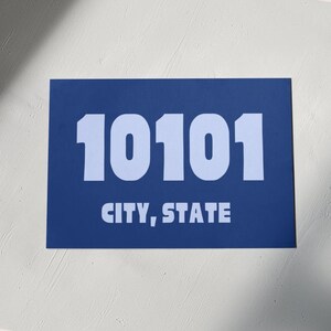Op de afbeelding: Een blauw rechthoekig bord met witte tekst. Het bord staat "10101 STAD, STAAT".