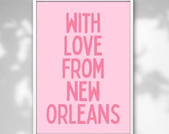 May include: A framed pink art print with the words "WITH LOVE FROM NEW ORLEANS" in a bold, pink font. The print is set against a white frame, creating a clean and modern aesthetic. The background is a light gray.