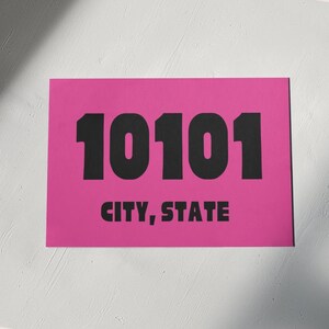 May include: A pink rectangular sign with the number 10101 printed in black bold font. The text "CITY, STATE" is printed below the number in black.