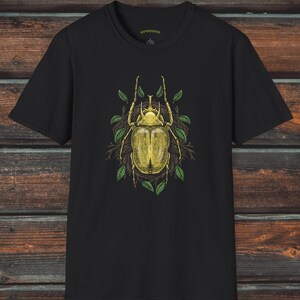 May include: Black t-shirt with a yellow beetle illustration surrounded by green leaves. The beetle has a detailed design and is set against a dark background. The text "Creepy Crawly Apparel" is visible in the top right corner.