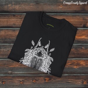 Op de afbeelding: Zwart T-shirt met een witte grafische print van een kever omringd door bladeren. De tekst "Creepy Crawly Apparel" is in wit bovenaan de afbeelding gedrukt.