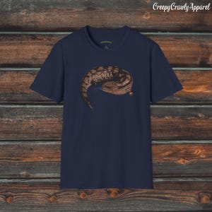 May include: A navy blue t-shirt with a brown and black lizard graphic. The lizard is curled up in a ball and has a blue tongue.