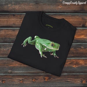 May include: Black t-shirt with a detailed illustration of a bright green frog. The frog has white markings and is positioned on the front. The text "Creepy Crawly Apparel" is visible in the upper right corner of the shirt.