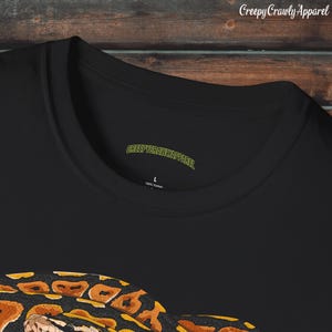 May include: Black t-shirt with a graphic print of a snake with orange and black markings. The shirt has a tag that says "CreepyCrawlyApparel" and "100% Cotton".