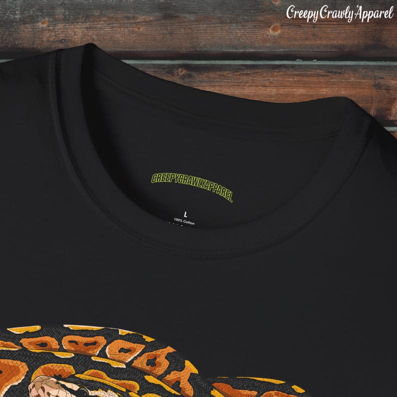 May include: Black t-shirt with a graphic print of a snake with orange and black markings. The shirt has a tag that says "CreepyCrawlyApparel" and "100% Cotton".