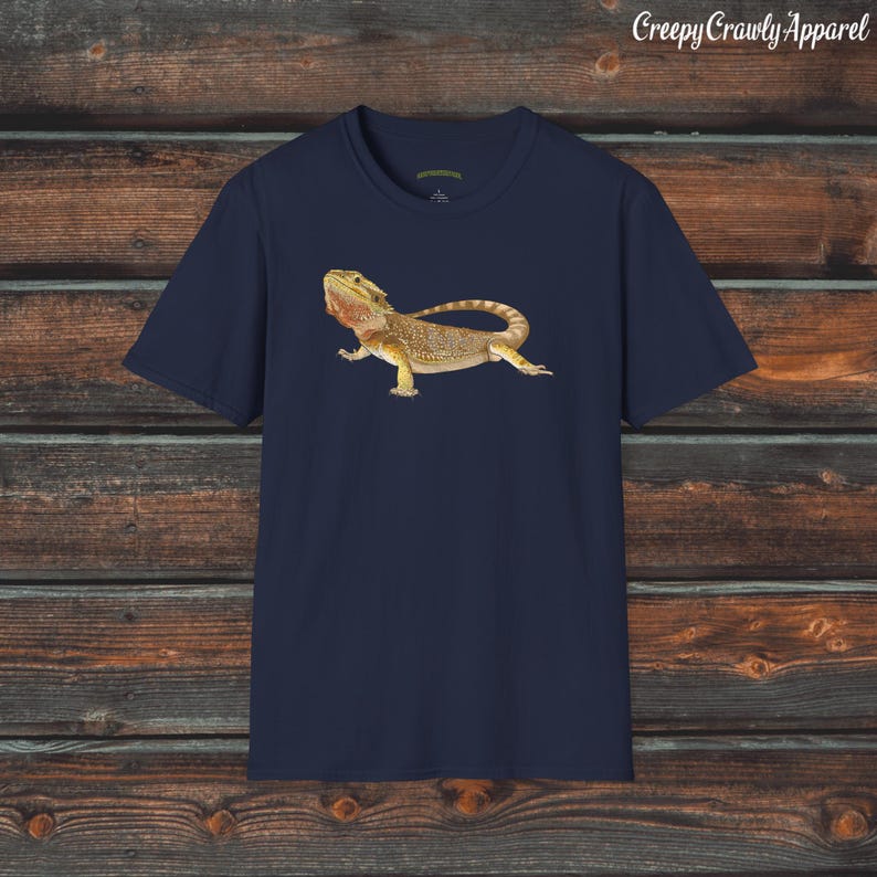 Op de afbeelding: Een donkerblauw t-shirt met een afbeelding van een baardagame. De hagedis is bruin, geel en oranje met een stekelige kam op zijn kop.