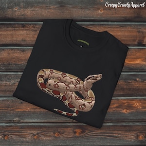 May include: Black t-shirt featuring a detailed illustration of a snake in shades of brown, tan, and red. The snake is coiled and positioned on the front of the shirt. The text "Creepy Crawly Apparel" is in the upper right corner.