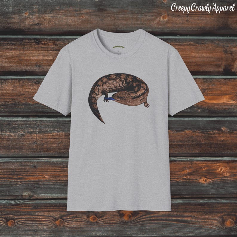 May include: A grey t-shirt with a brown and black lizard graphic. The lizard is curled up with its tail wrapped around its body. The text "Creepy Crawly Apparel" is printed in the top right corner of the image.