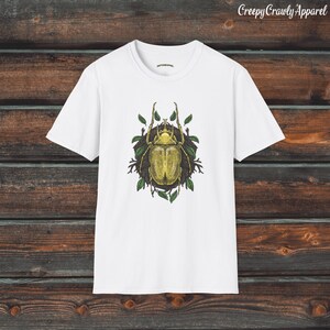 May include: White t-shirt with a graphic print of a green beetle surrounded by leaves.