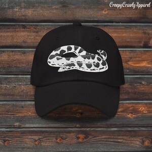 May include: Black baseball cap with a white and black snake illustration. The cap has a curved peak and a structured design. The text "Creepy Crawly Apparel" is printed in white on the upper right side of the cap.