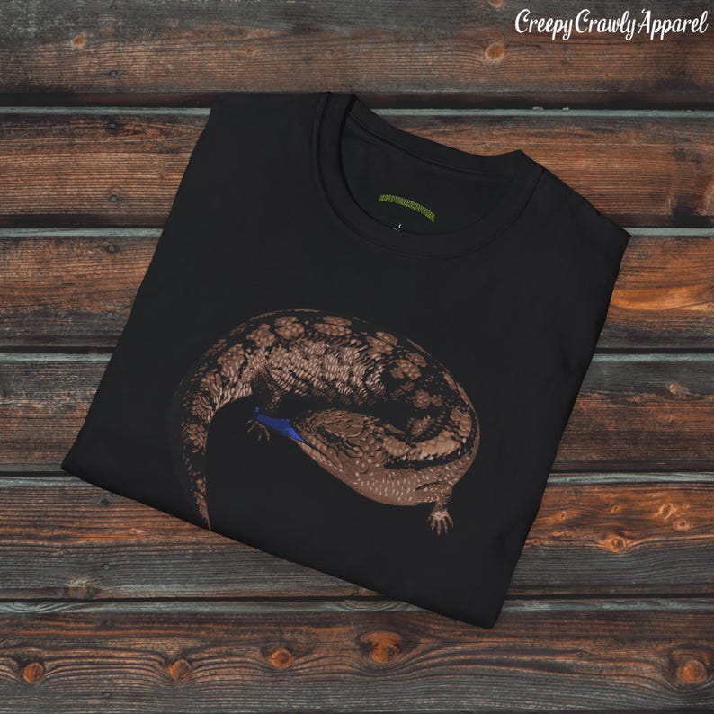 May include: Black t-shirt with a graphic print of a blue-tongued skink curled up on a black background. The text "Creepy Crawly Apparel" is printed in white at the top of the image.