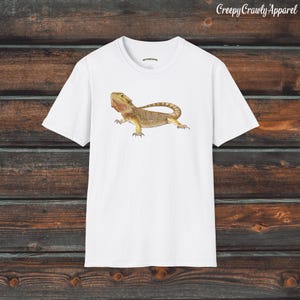 Op de afbeelding: Wit T-shirt met een afbeelding van een bruine en gele baardagame.