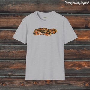 May include: A gray t-shirt with a graphic of a curled up snake with orange, black, and yellow markings. The snake is in the center of the shirt.