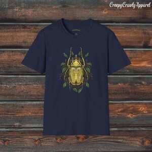 May include: Navy blue t-shirt with a yellow beetle illustration surrounded by green leaves. The beetle has a detailed design and is set against a dark background.