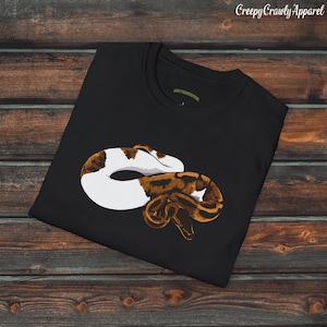 Peut inclure: T-shirt noir avec un motif de serpent brun et blanc enroulé. Le serpent a un ventre blanc et des marques brunes et orange.