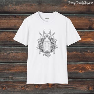 Op de afbeelding: Wit T-shirt met een zwart-witte illustratie van een kever omringd door bladeren.