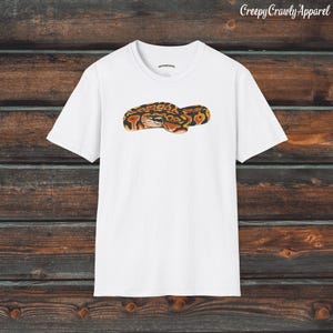 May include: White t-shirt with a graphic of a curled up snake with orange, brown, and black markings.