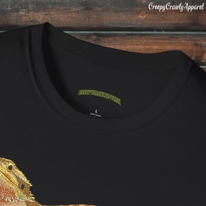 Op de afbeelding: Zwart T-shirt met een afbeelding van een baardagamenkop. Het shirt heeft een label met de tekst "CreepyCrawlyApparel" en "100% Katoen".