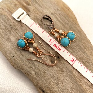 May include: A pair of turquoise and copper wire earrings with white beads. The earrings are approximately 1 inch long and are shown on a wooden surface with a ruler for scale.