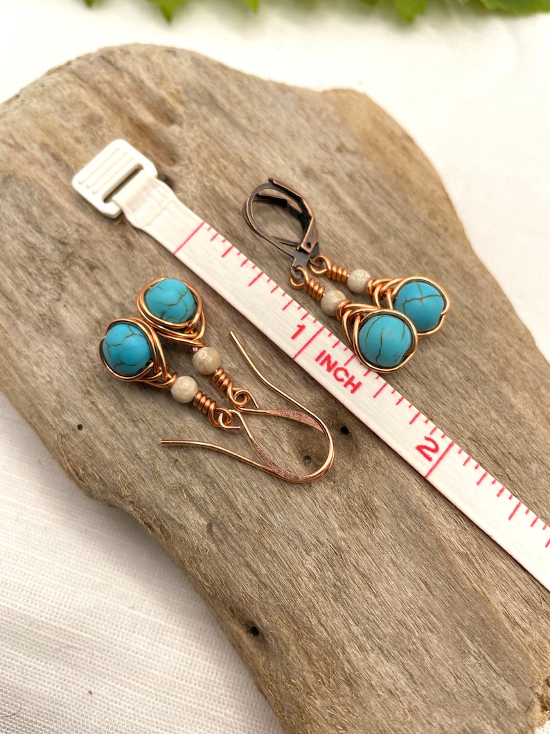 May include: A pair of turquoise and copper wire earrings with white beads. The earrings are approximately 1 inch long and are shown on a wooden surface with a ruler for scale.