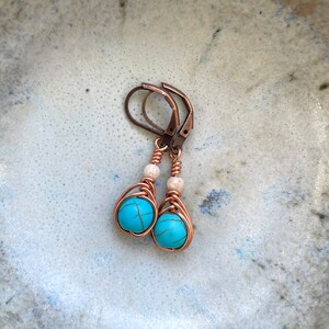 May include: A pair of turquoise and copper wire wrapped earrings with white beads. The earrings have a simple design and are perfect for everyday wear.