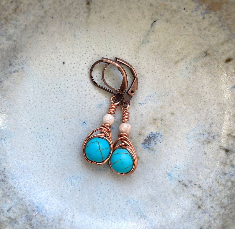 May include: A pair of turquoise and copper wire wrapped earrings with white beads. The earrings have a simple design and are perfect for everyday wear.