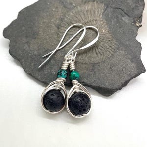 Peut inclure: Boucles d'oreilles en argent avec des perles de lave noire et turquoise. Les boucles d'oreilles sont enroulées de fil et ont un design simple.
